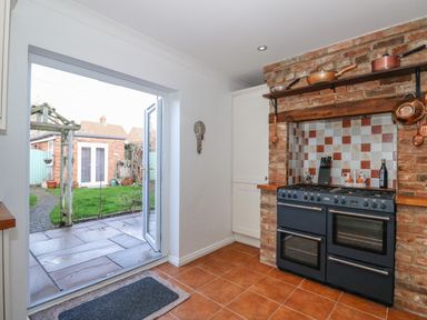 A kitchen with a double oven range and brick tiled backsplash next to an open door leading to a garden at Jobs Cottage in Snettisham