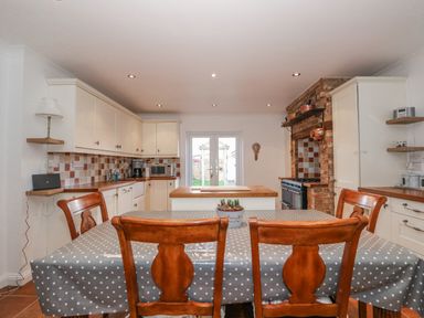 A kitchen with wooden chairs around a table covered with a polka dot tablecloth and cabinets along the walls at Job's Cottage in Snettisham