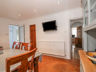 A dining area with wooden chairs and table with a polka dot tablecloth a wall-mounted TV and open doors at Job's Cottage in Snettisham