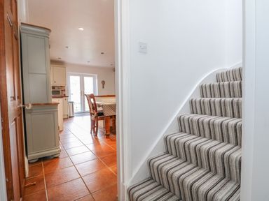 A striped carpeted staircase next to a kitchen with a wooden table and chairs at Job's Cottage in Snettisham