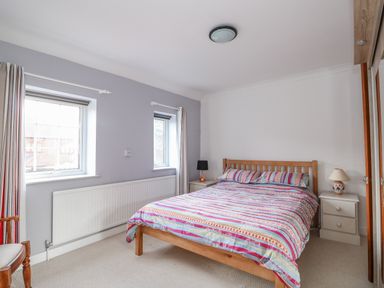 A bedroom with a bed with striped bedding two bedside tables with lamps two windows with curtains and a mirrored wardrobe at Job's Cottage in Snettisham