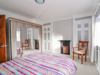 A bedroom with a bed with striped bedding a wooden chair a fireplace mirrored wardrobe and white closets at Job's Cottage in Snettisham