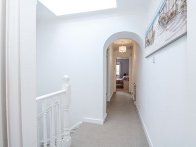 A hallway with a carpeted floor and white walls leading to a bedroom at Job's Cottage in Snettisham