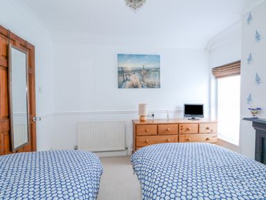 A bedroom with two single beds covered with blue patterned bedding a wooden dresser with a lamp and small TV a door with a mirror and a window with blinds at Job's Cottage in Snettisham