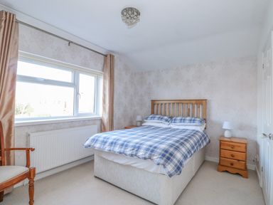 A bedroom with a double bed and wooden headboard two wooden bedside tables with lamps a window with curtains and a wooden chair at Job's Cottage in Snettisham