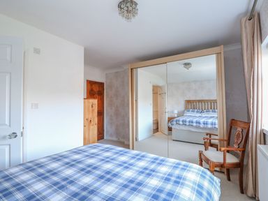 A bedroom with a bed covered in blue checkered bedding a wooden chair and mirrored wardrobe at Job's Cottage in Snettisham