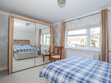 A bedroom with a bed, two wooden chairs, a large mirrored wardrobe, and windows with curtains at Job's Cottage in Snettisham