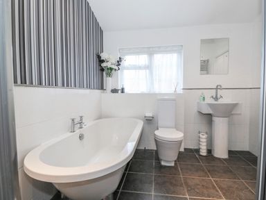 A bathroom with a bathtub toilet sink flowers and a window at Job's Cottage in Snettisham