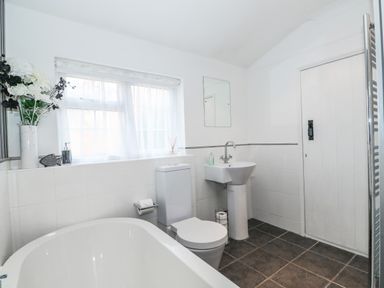A bathroom with a bathtub toilet pedestal sink mirror and window with flowers on the ledge at Job's Cottage in Snettisham
