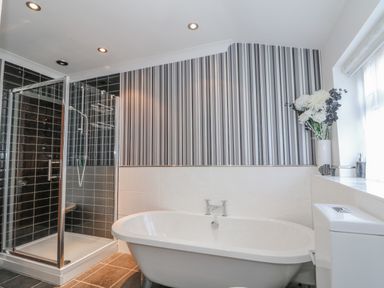A bathroom with a bathtub shower enclosure toilet and flowers in a vase on a windowsill at Job's Cottage in Snettisham