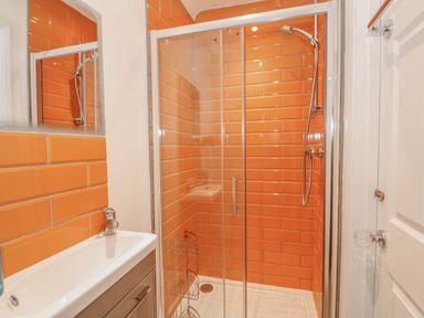 A shower with orange tiles and a sliding glass door next to a sink with a mirror above at Jobs Cottage in Snettisham