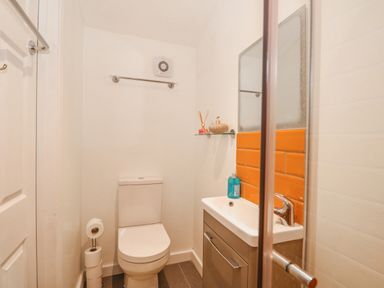 A small bathroom with a toilet, sink, mirror, and orange tiles at Job's Cottage in Snettisham