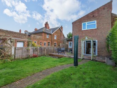A backyard with grass lawn a brick path a wooden pergola outdoor table and chairs and open double doors at Job's Cottage in Snettisham