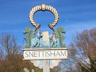 A wooden sign for Snettisham with two seahorses and two figures near water at Snettisham