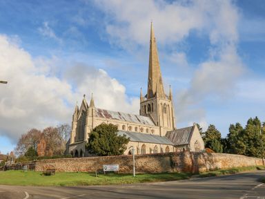 A church with a tall spire surrounded by a stone wall and trees at Job's Cottage in Snettisham