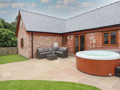 An outdoor patio with a wicker sofa set and a hot tub next to a brick house at The Clockhouse in Llandyssil near Montgomery