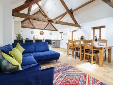 An open living and dining area with blue sofas and colorful rug and wooden dining table at The Clockhouse in Llandyssil near Montgomery