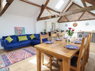 An open plan kitchen and dining area with a wooden dining table set for six and a blue sofa with green cushions at The Clockhouse in Llandyssil near Montgomery