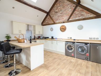 A kitchen with white cabinets wooden countertops bar stools and appliances at The Clockhouse in Llandyssil near Montgomery