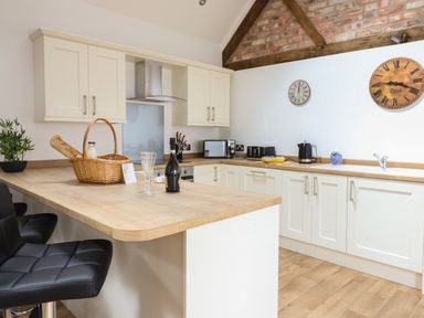 A kitchen with white cabinets wooden countertops black bar stools and two wall clocks at The Clockhouse in Llandyssil near Montgomery