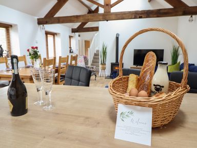 A dining room with a basket of bread eggs and milk on the table and a bottle with glasses at The Clockhouse in Llandyssil near Montgomery