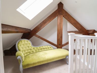 An attic space with wooden beams a green upholstered chaise lounge and a white railing at The Clockhouse Llandyssil near Montgomery