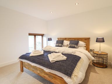 A bedroom with a wooden bed with white linens blue pillows and blankets two bedside tables with lamps and a window with wooden blinds at The Clockhouse in Llandyssil near Montgomery