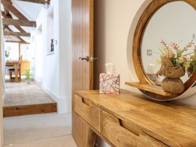 A wooden dressing table with a round mirror and a tissue box in a hallway leading to a dining area at The Clockhouse in Llandyssil near Montgomery