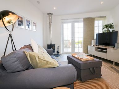 A living room with a gray sofa and cushions a floor lamp stove coffee table TV and sliding glass doors at Badgers Way in Tintagel