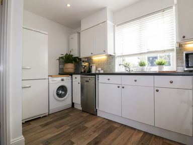 A kitchen with white cabinets washing machine dishwasher and refrigerator with plants on the countertop at Badgers Way in Tintagel