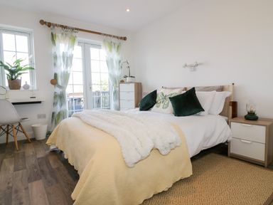 A bedroom with a bed with pillows and a blanket next to a window with sheer curtains and a dresser at Badgers Way in Tintagel