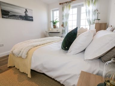 A bedroom with a bed a desk and windows with curtains at Badgers Way in Tintagel