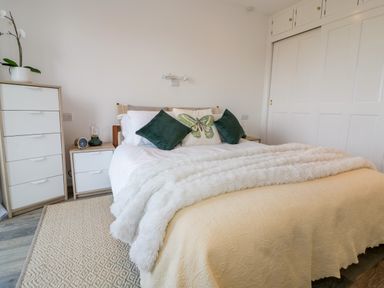 A bedroom with a bed featuring pillows and a furry blanket a dresser with a plant and a nightstand with a clock at Badgers Way in Tintagel