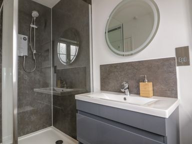 A bathroom with a shower enclosure and a sink with a faucet and soap dispenser at Badgers Way in Tintagel