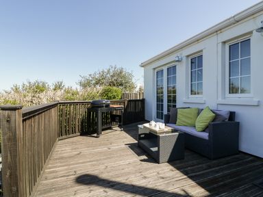 A wooden deck with a black barbecue grill and a rattan sofa with green and gray cushions at Badgers Way in Tintagel