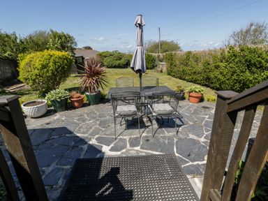 A garden patio with a table and chairs with an umbrella and potted plants at Badgers Way in Tintagel