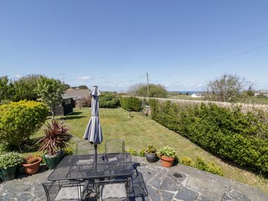 A garden with patio furniture and an umbrella surrounded by plants and a lawn at Badgers Way in Tintagel