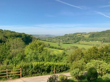 A view of green fields trees and hills under a blue sky at Under Catswood in Elcombe near Stroud