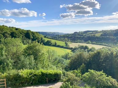 A landscape with green trees and fields under a blue sky with clouds at Under Catswood in Elcombe near Stroud
