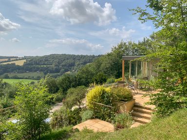 A patio with outdoor furniture and plants overlooking a valley with trees at Under Catswood in Elcombe near Stroud