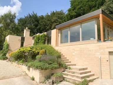 A modern house with large windows and steps surrounded by shrubs and trees at Under Catswood in Elcombe near Stroud