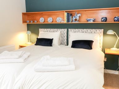 A bedroom with two single beds with white bedding and black cushions under a wooden shelf with decorative items at Under Catswood in Elcombe near Stroud