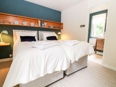 A bedroom with two beds side by side with white bedding pillows and folded towels a teal accent wall with wooden shelves holding plates and books Under Catswood Elcombe near Stroud