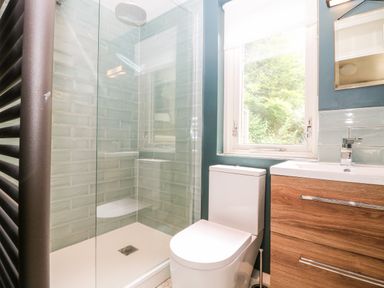 A bathroom with a glass shower enclosure toilet and wooden vanity unit under a window at Under Catswood in Elcombe near Stroud