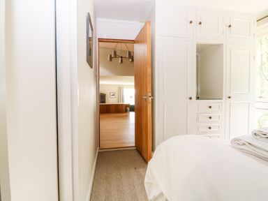 A bedroom with white built in wardrobes a wooden door open to a living room at Under Catswood in Elcombe near Stroud