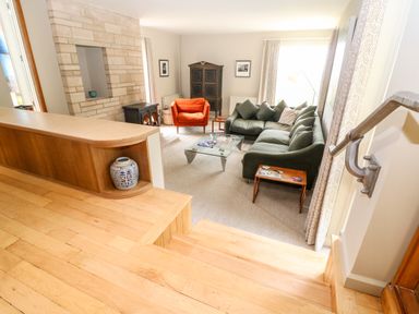 A living room with a green sofa an orange armchair a glass coffee table a fireplace and wooden stairs at Under Catswood in Elcombe near Stroud