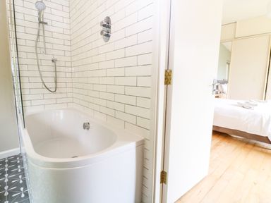 A bathroom with a bathtub and shower head next to a bedroom with a bed and towels at Under Catswood in Elcombe near Stroud