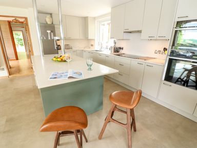 A kitchen with a green island and two brown stools at Under Catswood in Elcombe near Stroud