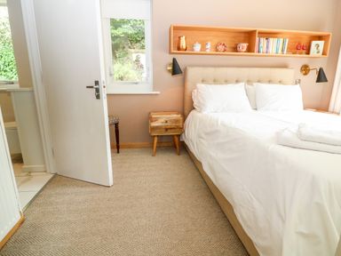 A bedroom with a bed white bedding wooden bedside table wall-mounted shelf with books and decor at Under Catswood in Elcombe near Stroud