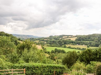A view of rolling green hills and fields with trees under a cloudy sky at Under Catswood in Elcombe near Stroud